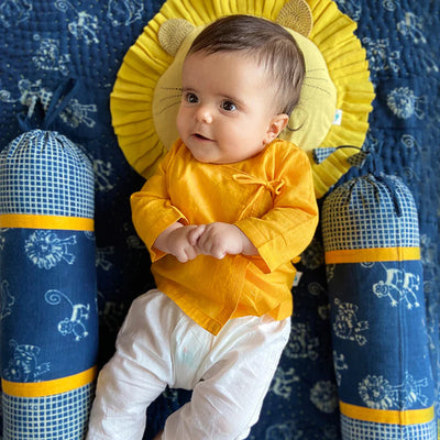 A baby wearing a yellow dress, laying on a bed.