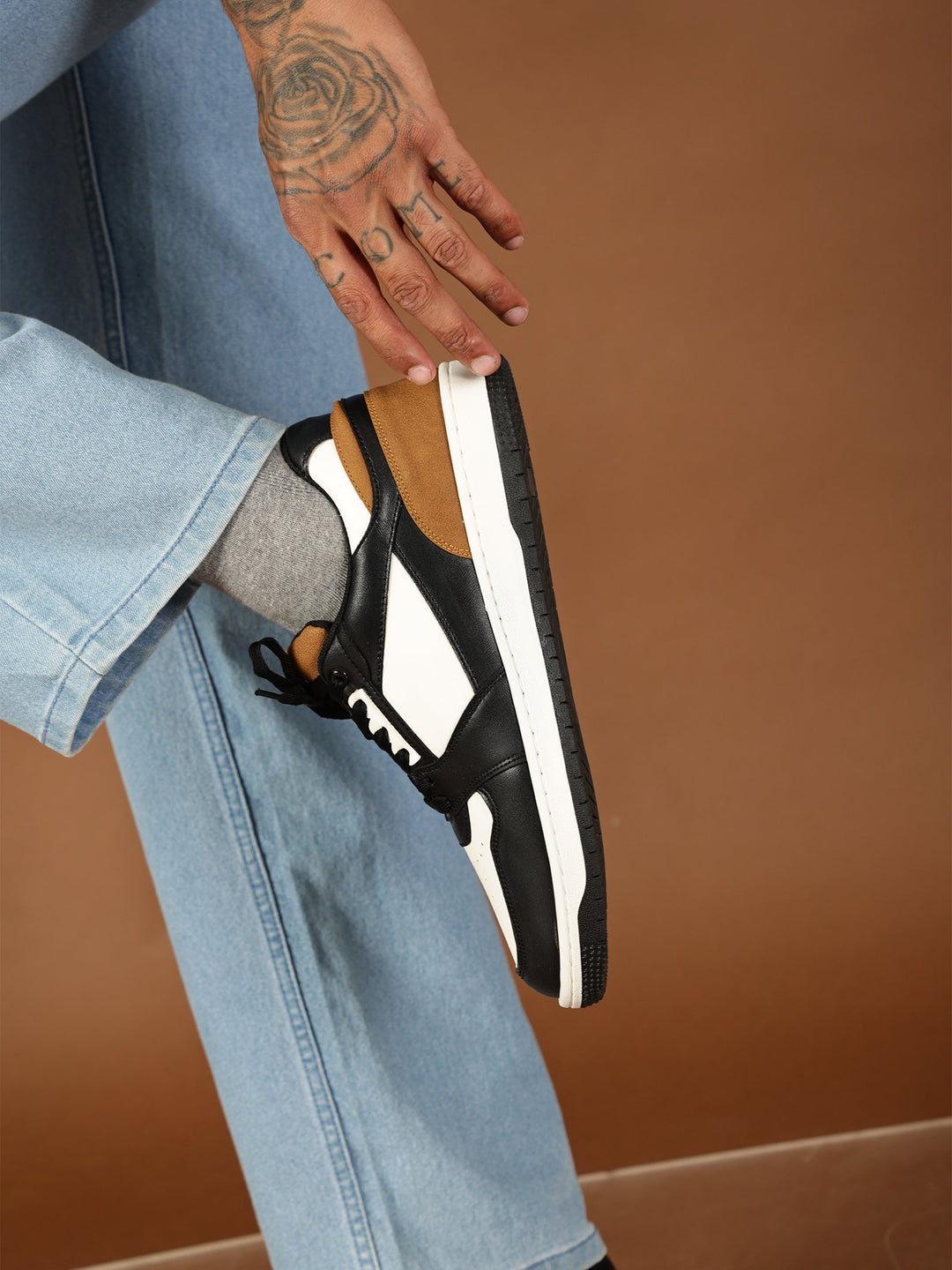 Person holding a black sandal with white sole against a brown background