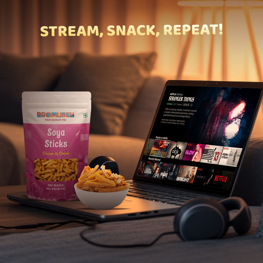 Soya Sticks in Cream & Onion flavor displayed alongside a bowl of snacks, a laptop streaming a show, and headphones, capturing a cozy binge-watching setup with the tagline &
