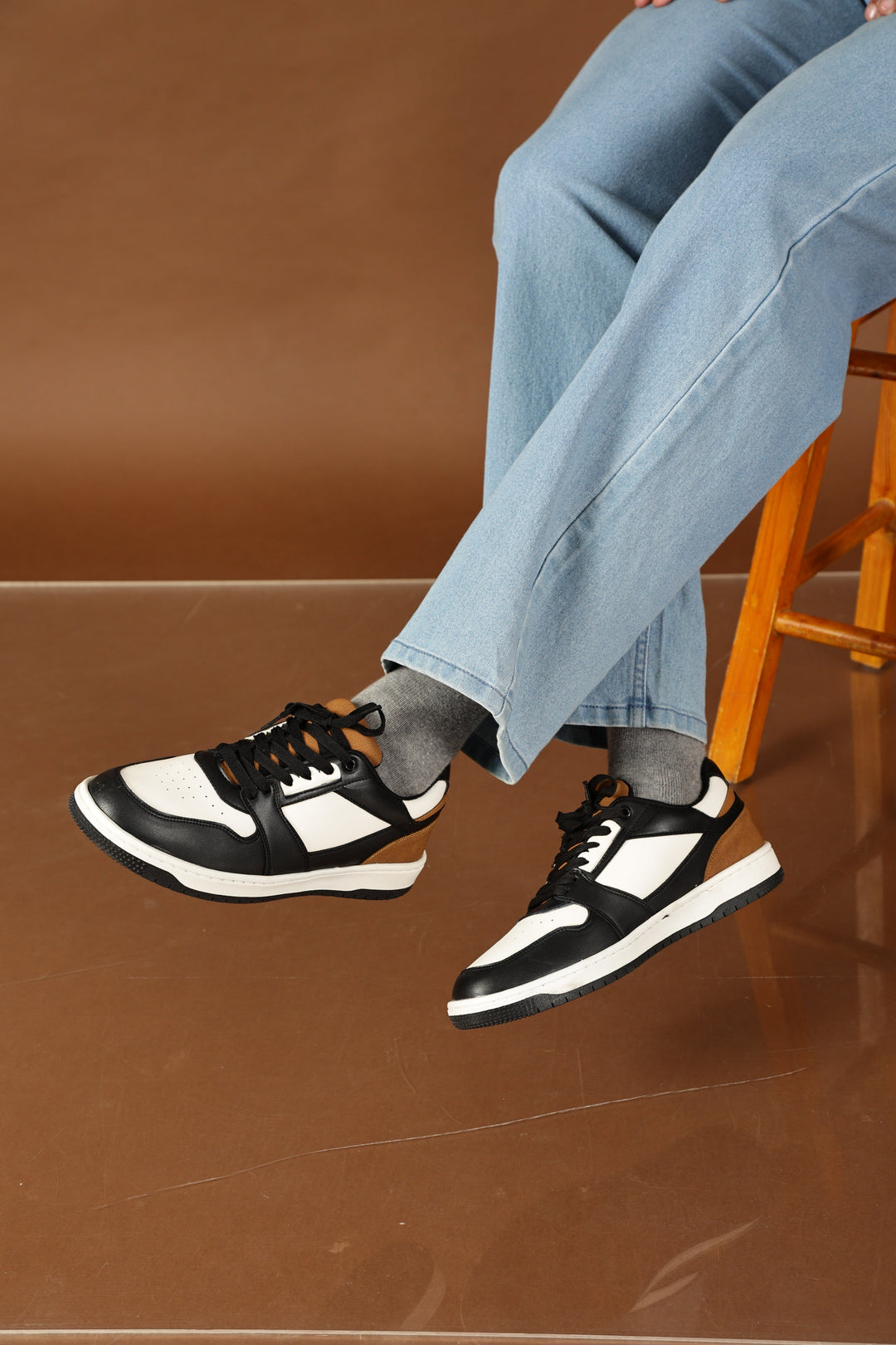 Person wearing black and white sneakers and light blue jeans sitting on a chair with a brown background