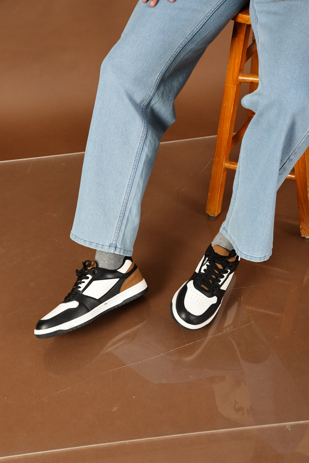 Person wearing black and white sneakers and light blue jeans against a brown background
