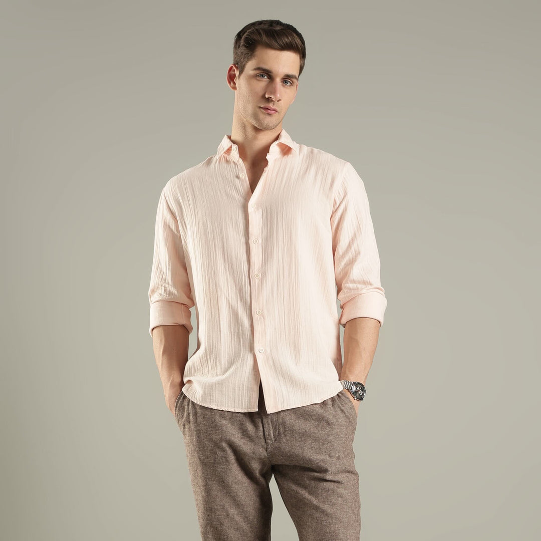 Man wearing a light pink shirt and gray pants against a plain background