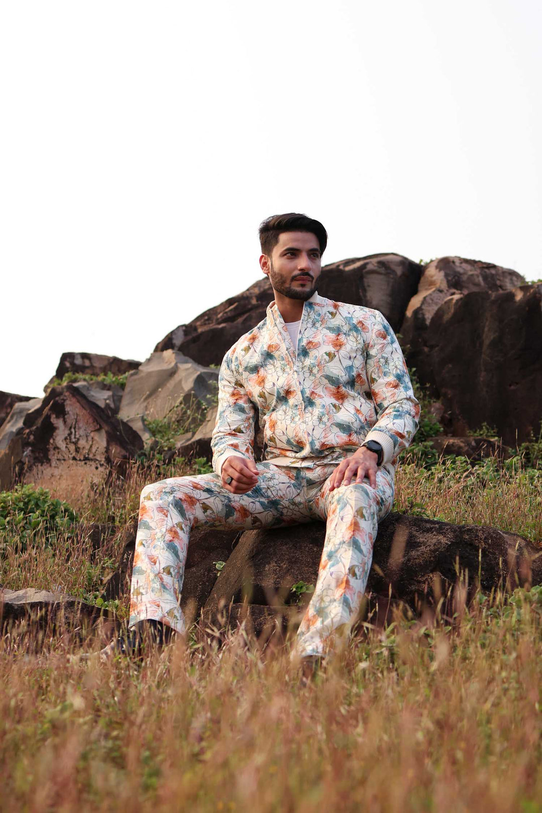 A man standing against a white background wearing a multicolored floral hemp bomber jacket with a round neckline and a front zipper.